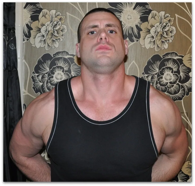 A clean-shaven, muscular man in a black tank top